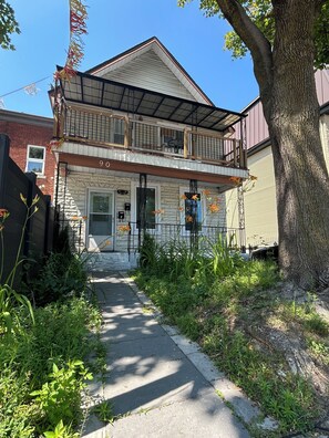 A two-story house with a balcony, a visible number '90' on the front, and a pathway leading to the entrance.