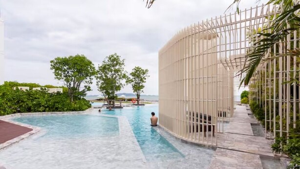 A swimming pool with a person in the water, surrounded by greenery and a white fence. - Family Suite Sea view 2Bedroom  (Pattaya)