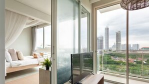 A modern bedroom with a bed, a TV on a wooden stand, and a balcony with a city view. - Family Suite Sea view 2Bedroom  (Pattaya)