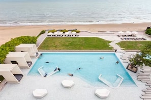 Área de piscina com espreguiçadeiras e guarda-sóis, vista para a praia e gramado.