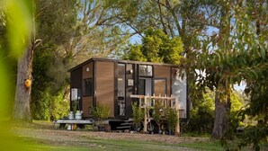 A modern, two-story cabin with a deck, surrounded by trees and a grassy area. - Orange 2 by Tiny Away (Woori Yallock)