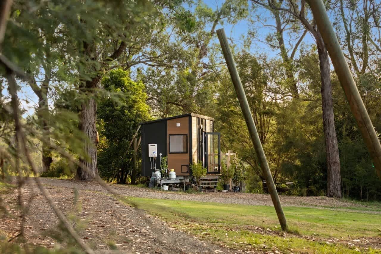 A small, modern cabin with a large window and a door, surrounded by trees.