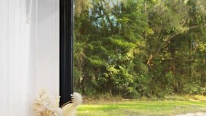 A modern kitchen with a stainless steel sink, a vase of flowers, and a window offering a view of a green landscape. - Orange 2 by Tiny Away (Woori Yallock)
