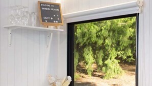 A kitchen with a wooden countertop, a sink, a dishwasher, a window with a view of trees, and a welcome sign. - Orange 2 by Tiny Away (Woori Yallock)