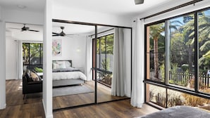 A modern bedroom with a large sliding glass door leading to a balcony, a ceiling fan, and a bed with a view of the outdoors.