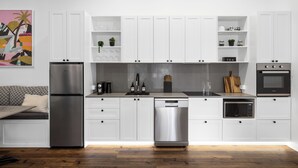 A modern kitchen with white cabinets, stainless steel appliances, and a wooden floor.