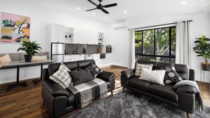 A modern living room with two black leather sofas, a dining table, and a kitchen in the background.
