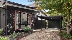 A modern house with a large glass window, a covered patio, and a garden with gravel and plants.