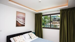 Une chambre à coucher avec un lit, un tableau, une fenêtre avec des rideaux et une vue sur un espace extérieur comprenant des rochers et des palmiers.