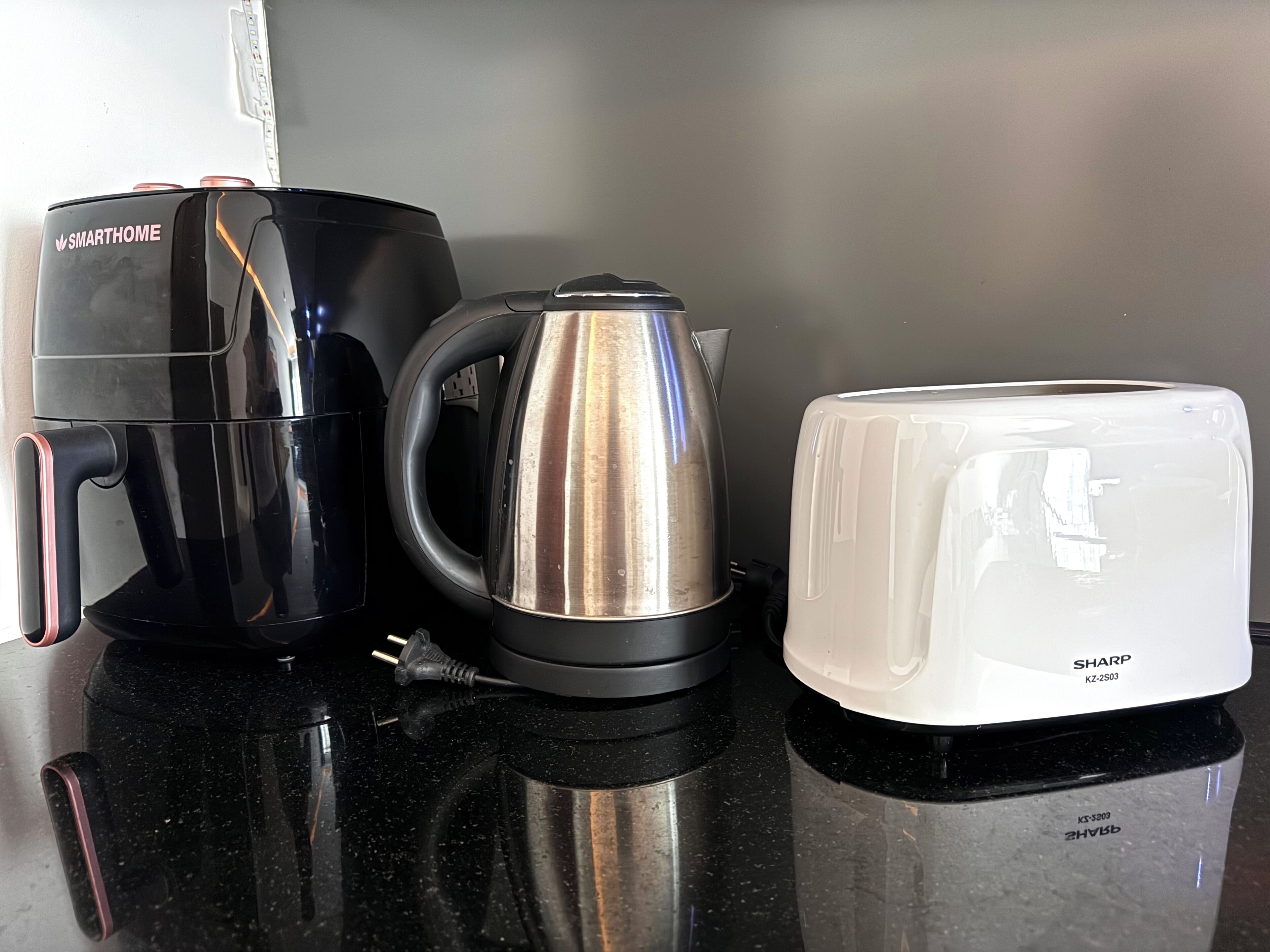 Un piano di lavoro in cucina con una macchina da caffè nera, un bollitore in acciaio inossidabile e un tostapane bianco.