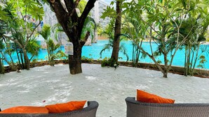 Un espace aménagé au bord de la piscine, avec des fauteuils en osier et des coussins orange, entouré d’une végétation luxuriante et offrant une vue sur la piscine.