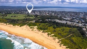 Luchtbeeld van een kustgebied met een strand, een golfbaan en een woongebied.