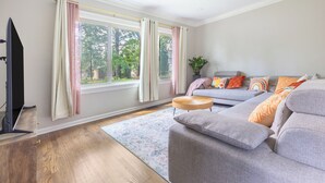 Ein modernes Wohnzimmer mit grauem Sofa, einem Flachbildfernseher und einem großen Fenster mit Vorhängen.