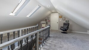 Ein geräumiges Dachzimmer mit hohen Decken, Dachfenstern, einer weißen Tür und einem schwarzen Stuhl.