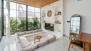 A modern living room with a large window, a sofa, a TV, and a dining area. - Bucu Villa by Betterplace (Kerobokan)