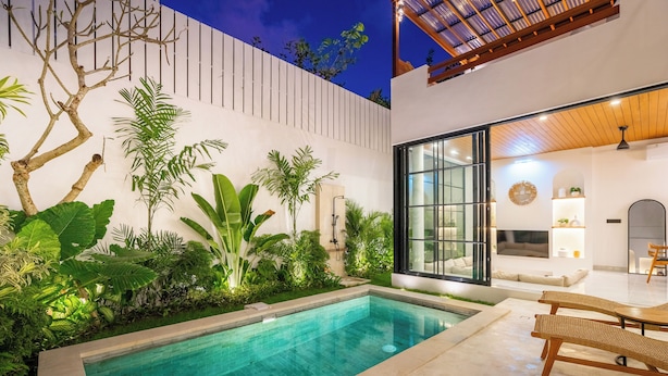 A modern outdoor pool area with a glass wall, wooden deck, and lush greenery. - Bucu Villa by Betterplace (Kerobokan)
