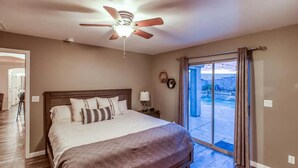 Une chambre avec un grand lit, un ventilateur de plafond, une table de chevet et une vue sur l’extérieur, accessible par une porte-fenêtre coulissante.