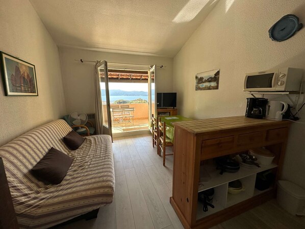 A compact living space with a sofa, a dining table, a kitchenette, and a balcony with a view.