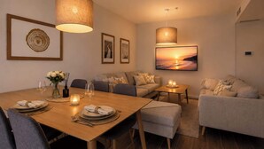 A modern living room with a wooden dining table, grey sofas, and a large TV mounted on the wall. - Jardines Guadaiza 2 | Sea Views Terrace Bbq (Marbella)