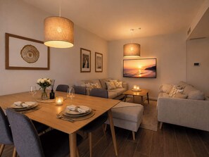 Ein modernes Wohnzimmer mit einem Holzesstisch, grauen Sofas und einem großen, an der Wand befestigten Fernseher.