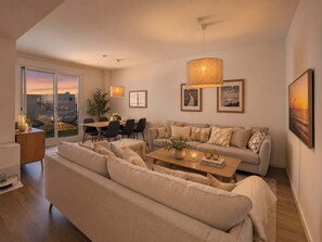 Un salon moderne avec un canapé, une table à manger et des chaises. Les murs sont ornés de tableaux encadrés, et de grandes fenêtres offrent une vue sur la ville.