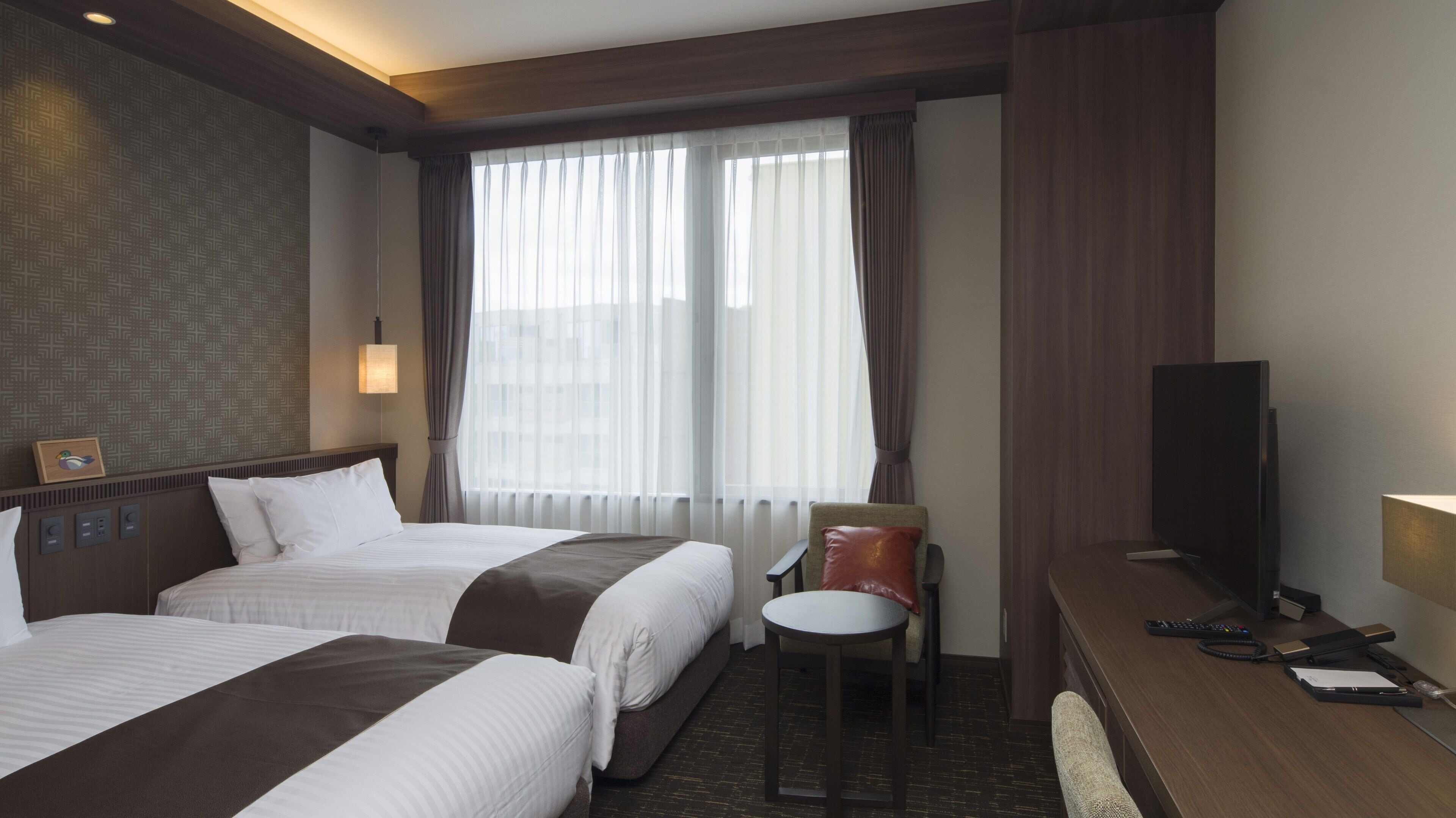 A hotel room with two beds, a desk, a chair, a television, and a window with curtains.