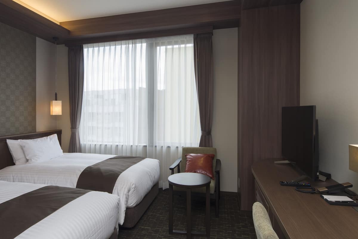 Habitación de hotel con dos camas, un escritorio, una silla, un televisor y una ventana con cortinas.