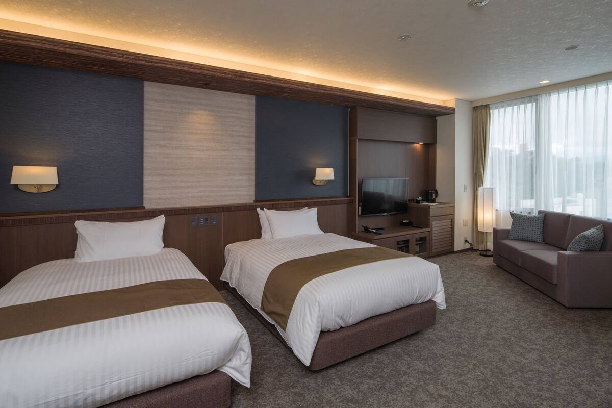 Une chambre d’hôtel avec deux lits, une télévision, un canapé et un bureau avec une lampe.