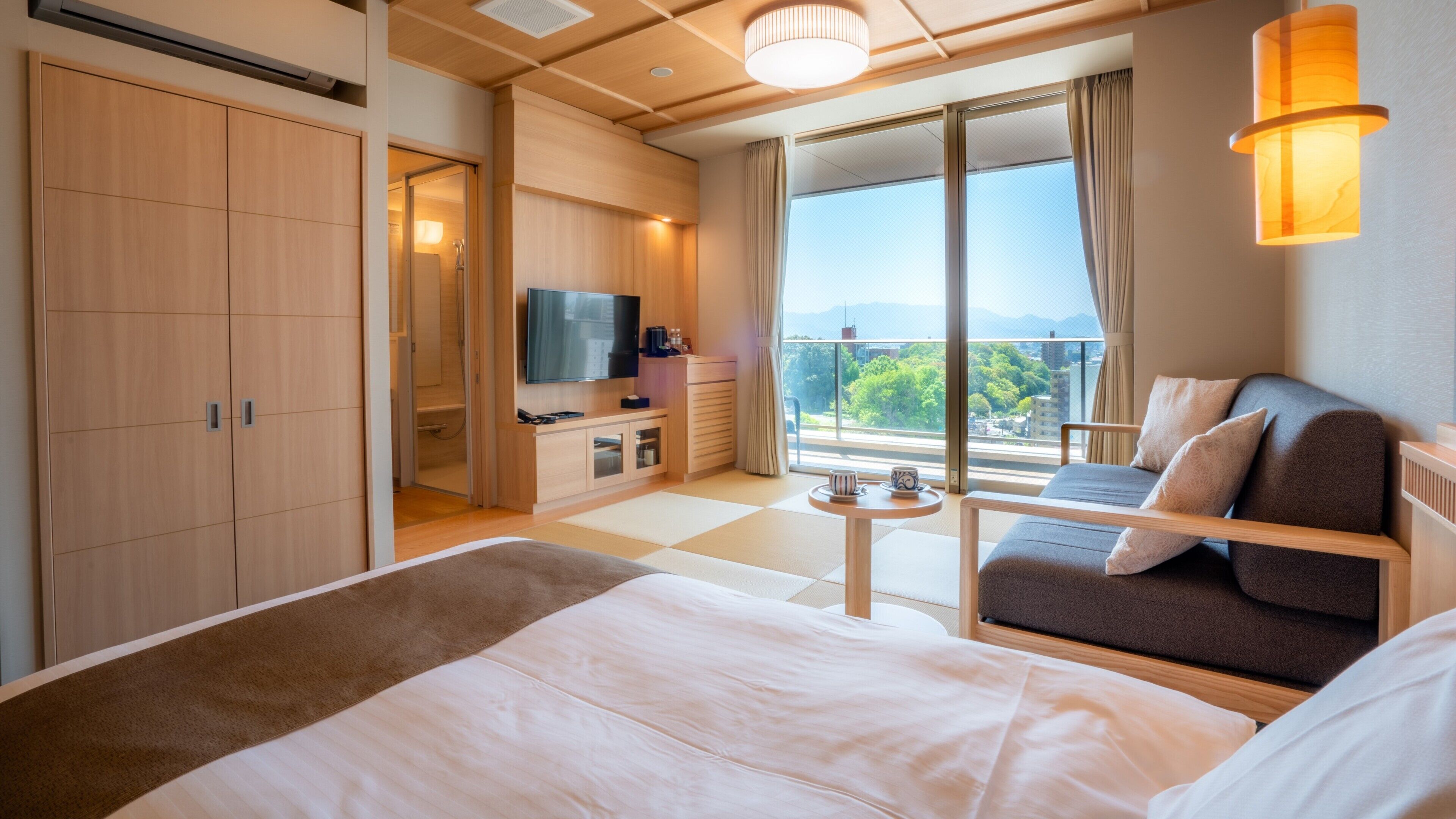 A modern hotel room with a large bed, a sofa, a TV, and a balcony with a view.