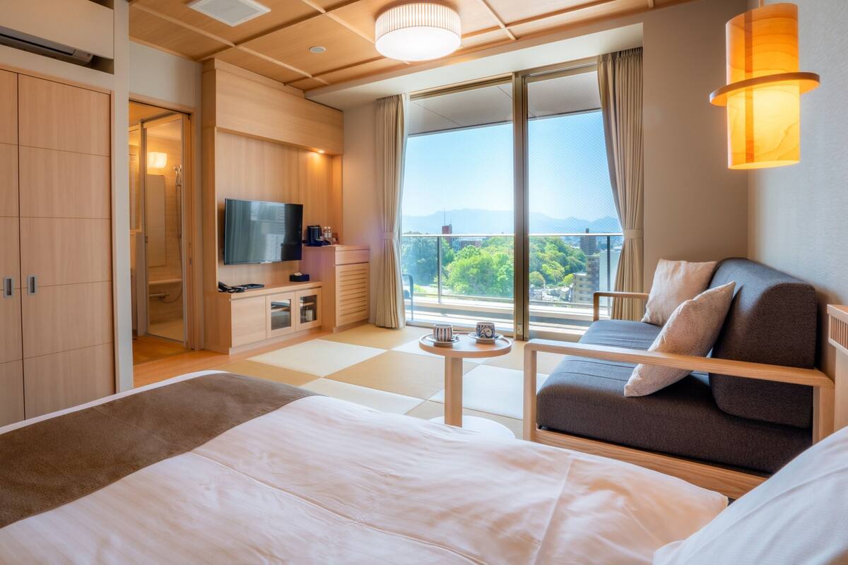A modern hotel room with a large bed, a sofa, a TV, and a balcony with a view.