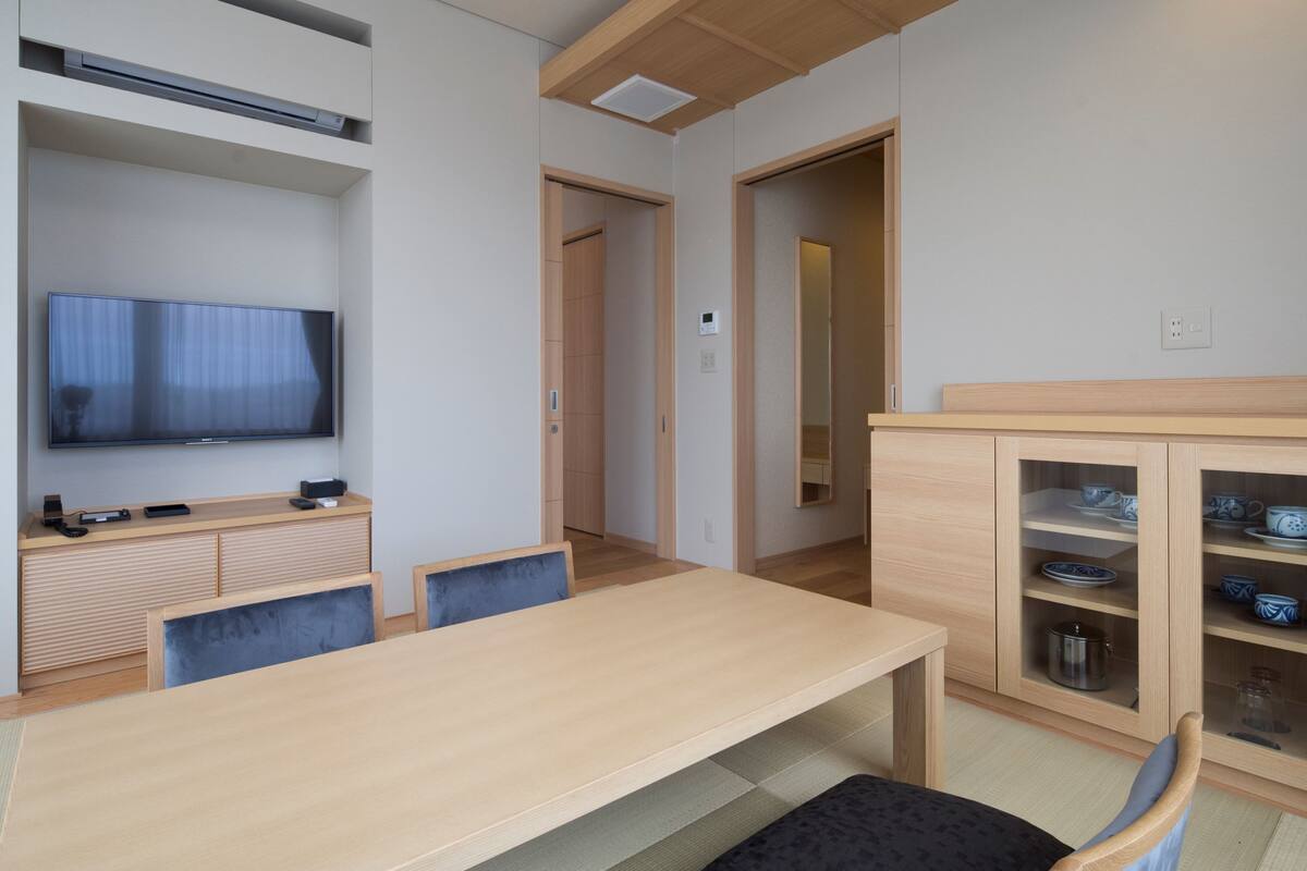 A modern living room with a flat-screen TV, wooden furniture, and a dining area with a table and chairs.