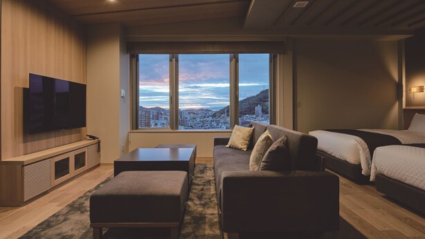 Une chambre d’hôtel moderne dotée d’une grande fenêtre, d’un téléviseur à écran plat, d’un canapé, d’un lit et d’une petite table.