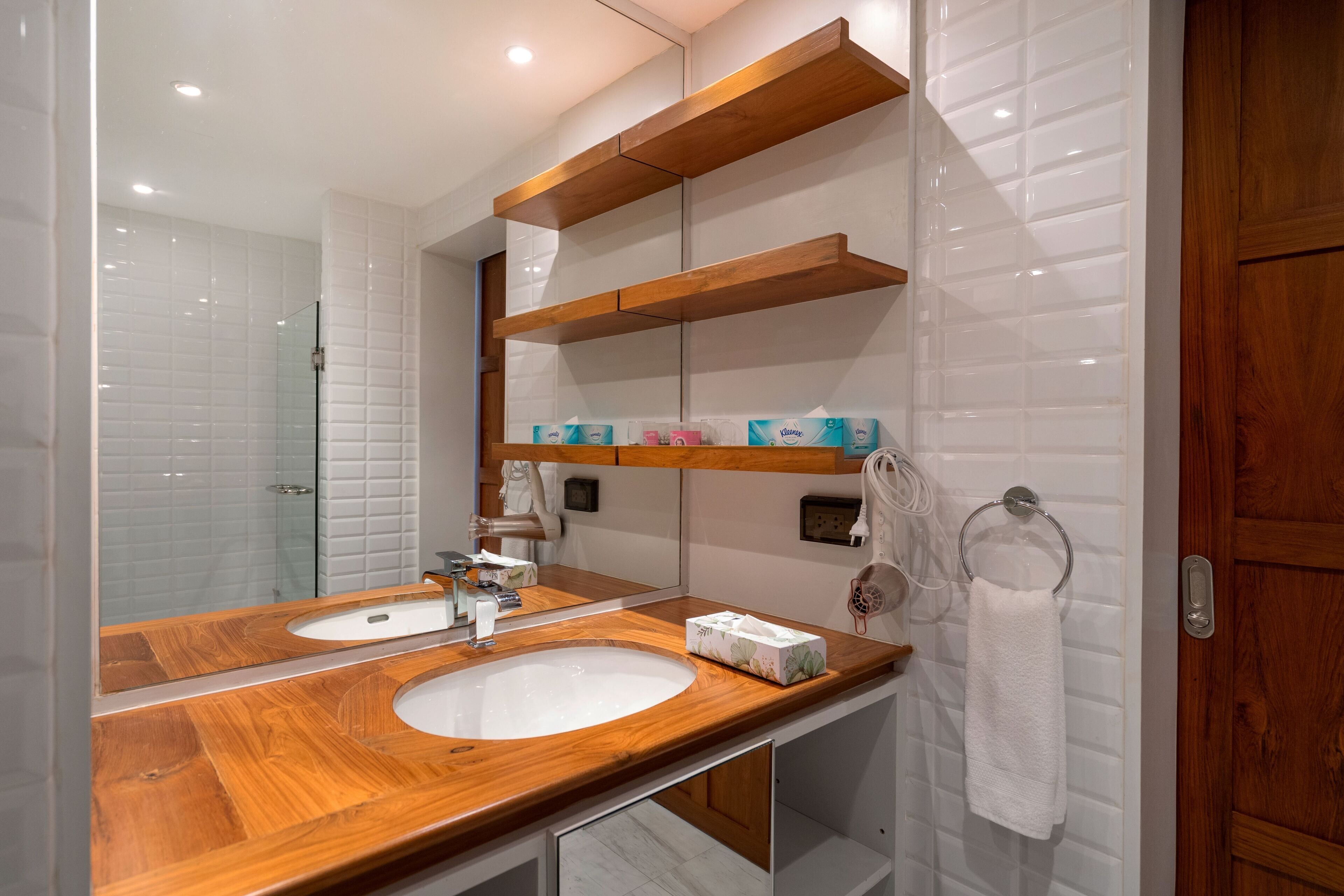 A bathroom with two sinks, wooden shelves, a towel rack, and a mirror.