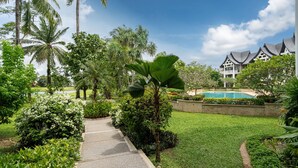 Un jardin luxuriant avec un sentier menant à une zone de piscine, entourée de palmiers et d’une végétation bien entretenue.