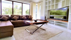 Un salon moderne avec un canapé d’angle, une table basse et un téléviseur à écran plat fixé au mur, lequel est décoré d’un motif en forme de quadrillage.