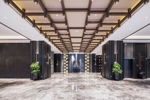 Un vestíbulo de hotel con suelo de mármol, iluminación moderna y una obra de arte central.