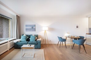 A modern living room with a sofa, coffee table, floor lamp, and dining area with chairs.