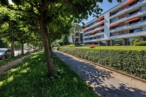 Ein mehrstöckiges Gebäude mit Balkonen, einem gepflasterten Weg und einer gepflegten Hecke.