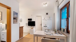 A modern, well-lit room with a dining table set for two, a television, and a window with blinds. - Apartment 'Ferienwohnung Strandquartier' with Private Terrace and Wi-Fi (Lübeck Travemünde)
