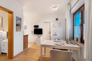 A modern, well-lit room with a dining table set for two, a television, and a window with blinds.