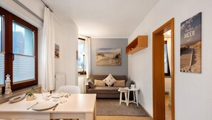 A compact living space with a dining area, a sofa, a small table, and a view of the outdoors. - Apartment 'Ferienwohnung Strandquartier' with Private Terrace and Wi-Fi (Lübeck Travemünde)