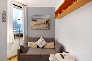A living room with a sofa, a painting of a beach, a lamp, and a shelf with shoes.