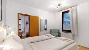 A bedroom with two beds, a mirror, a chair, and a window with curtains. - Apartment 'Ferienwohnung Strandquartier' with Private Terrace and Wi-Fi (Lübeck Travemünde)