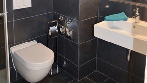 A bathroom with dark tiles, a white toilet, a sink with a mirror, and a sign with beach house rules.
