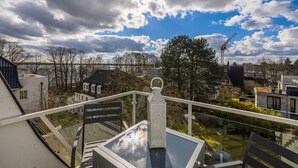 Un balcon doté d’une table et de chaises en verre, donnant sur un quartier résidentiel avec des maisons et des arbres.