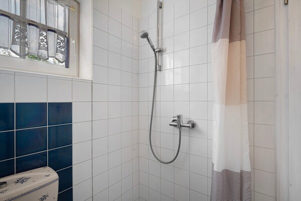 Une douche équipée d’un pommeau de douche à main, d’un robinet mural et d’un rideau de douche.