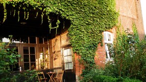 A brick building with ivy-covered walls, a cobblestone courtyard, and wooden furniture. - Room 'Blaues Zimmer' with Shared Garden and Wi-Fi (Schlagsdorf)