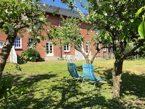 Ein Backsteinhaus mit Rasen, zwei blauen Stühlen und einem Baum mit weißen Blüten.