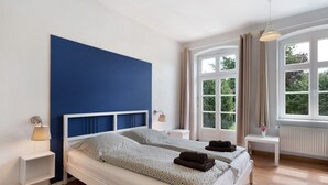 A bedroom with a large bed, bedside tables, a window with curtains, and a view of greenery outside. - Room 'Blaues Zimmer' with Shared Garden and Wi-Fi (Schlagsdorf)