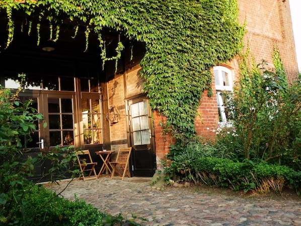 A brick building with ivy-covered walls, a cobblestone courtyard, and wooden furniture.